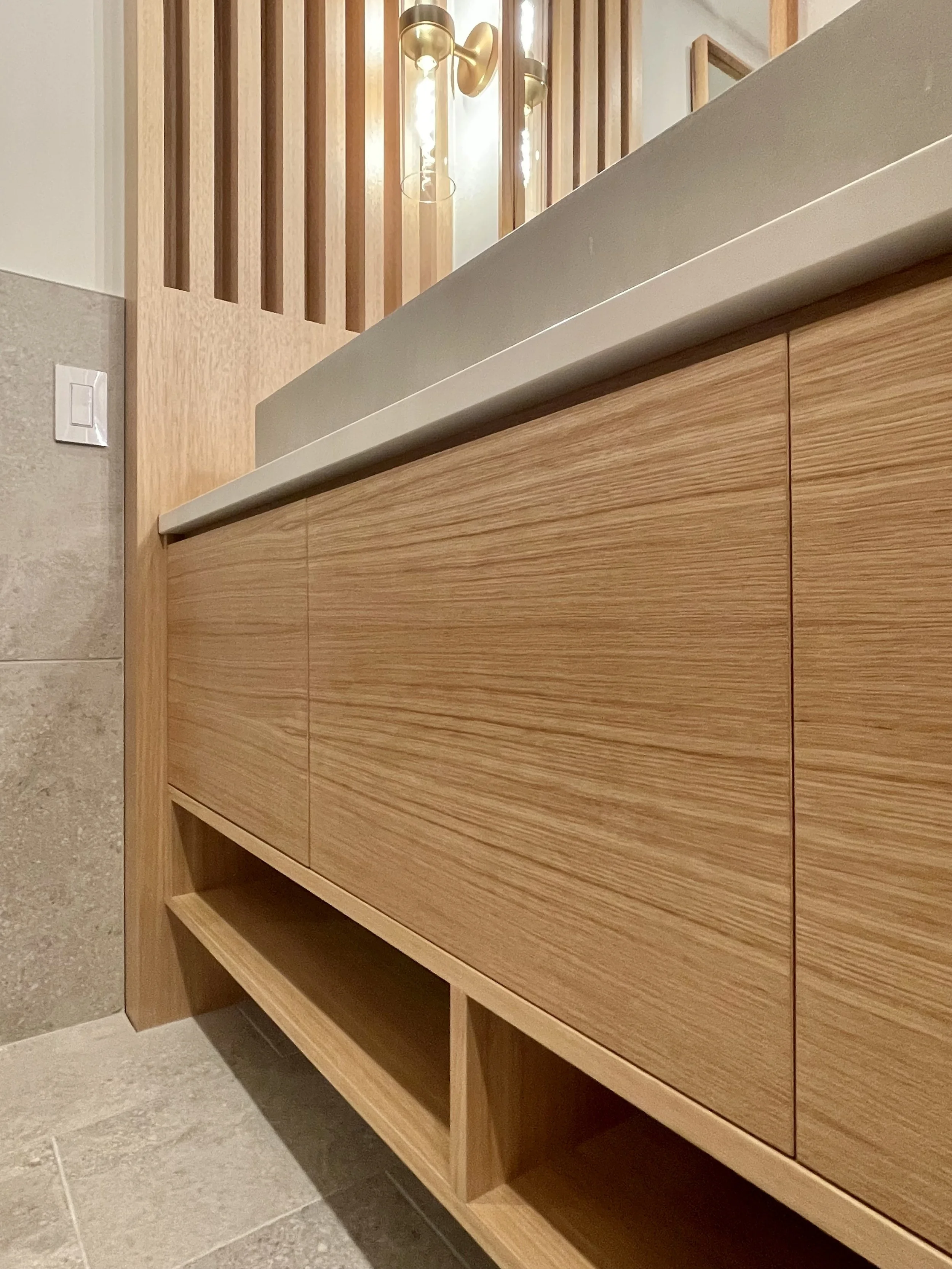 Architectural Detail of Floating Custom Vanity Base in Uniform Hickory Veneer and Hickory Heartwood Finished with Centurion 2K Polyurethane.

Wall Mounted Lighting Fixtures are Kohler Purist in Vibrant Brushed Modern Gold. 

TrueForm Custom Concrete 
