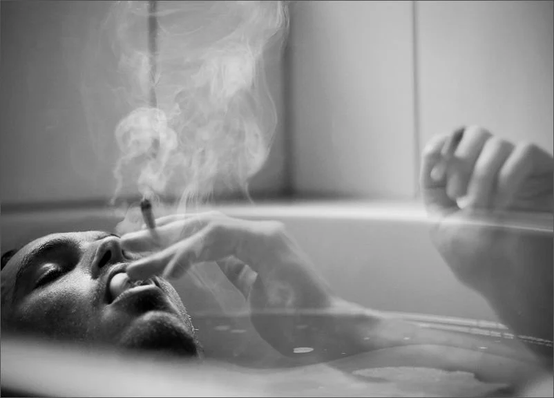 ein junger mann liegt in der badewanne ud genießt einen joint in der heißen wanne. er ist sichtlich entspannt.