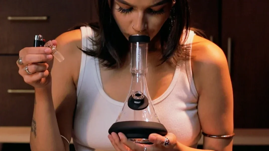 Eine junge Frau raucht den Deco Beaker von GRAV in Silikon und genießt den Zug an der premium bong ersichtlich.