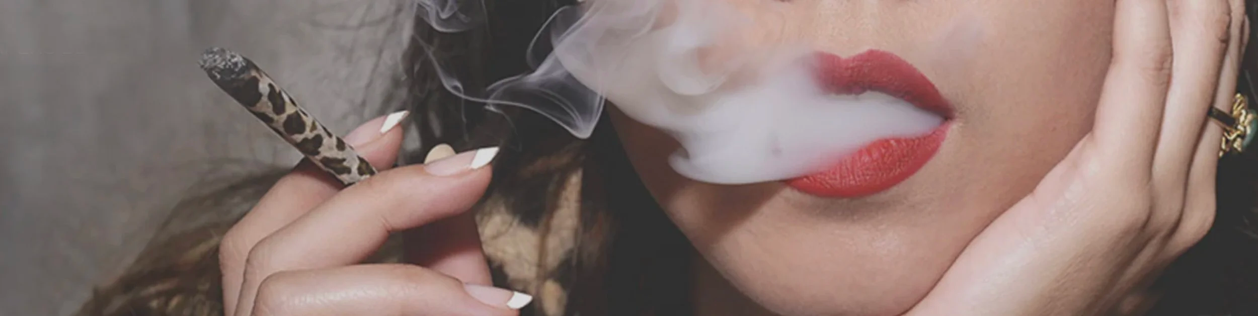 Eine frau die Qualm aus Ihrem mit rotem lippenstift bemalten Mund austrtetn lässt. Sie hält eine Jont mit leopard ChuChu papers von paers &Ink in ihrer Hand.