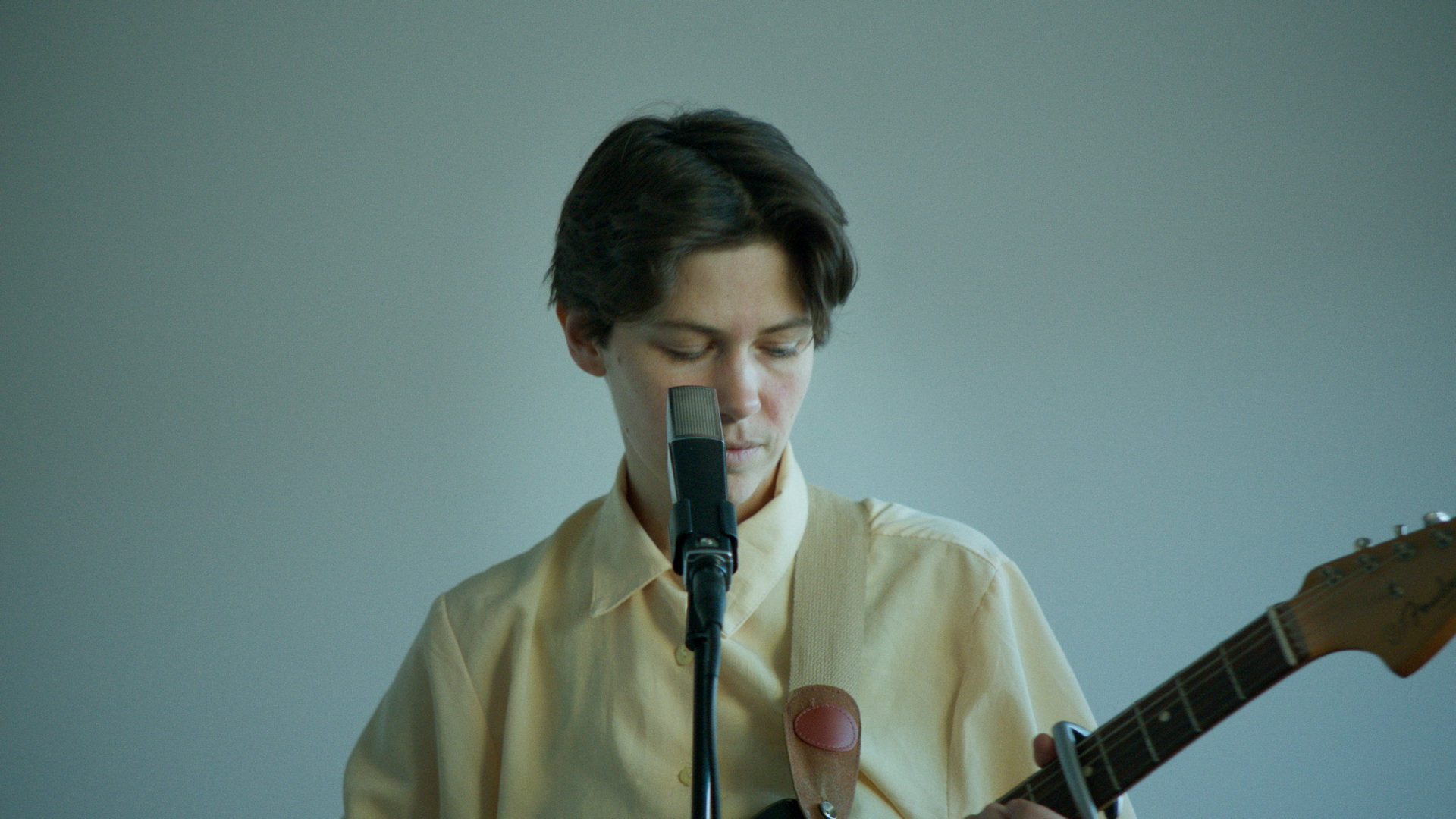 Junge Person singt in einem Mikrofon, während sie Gitarre spielt.