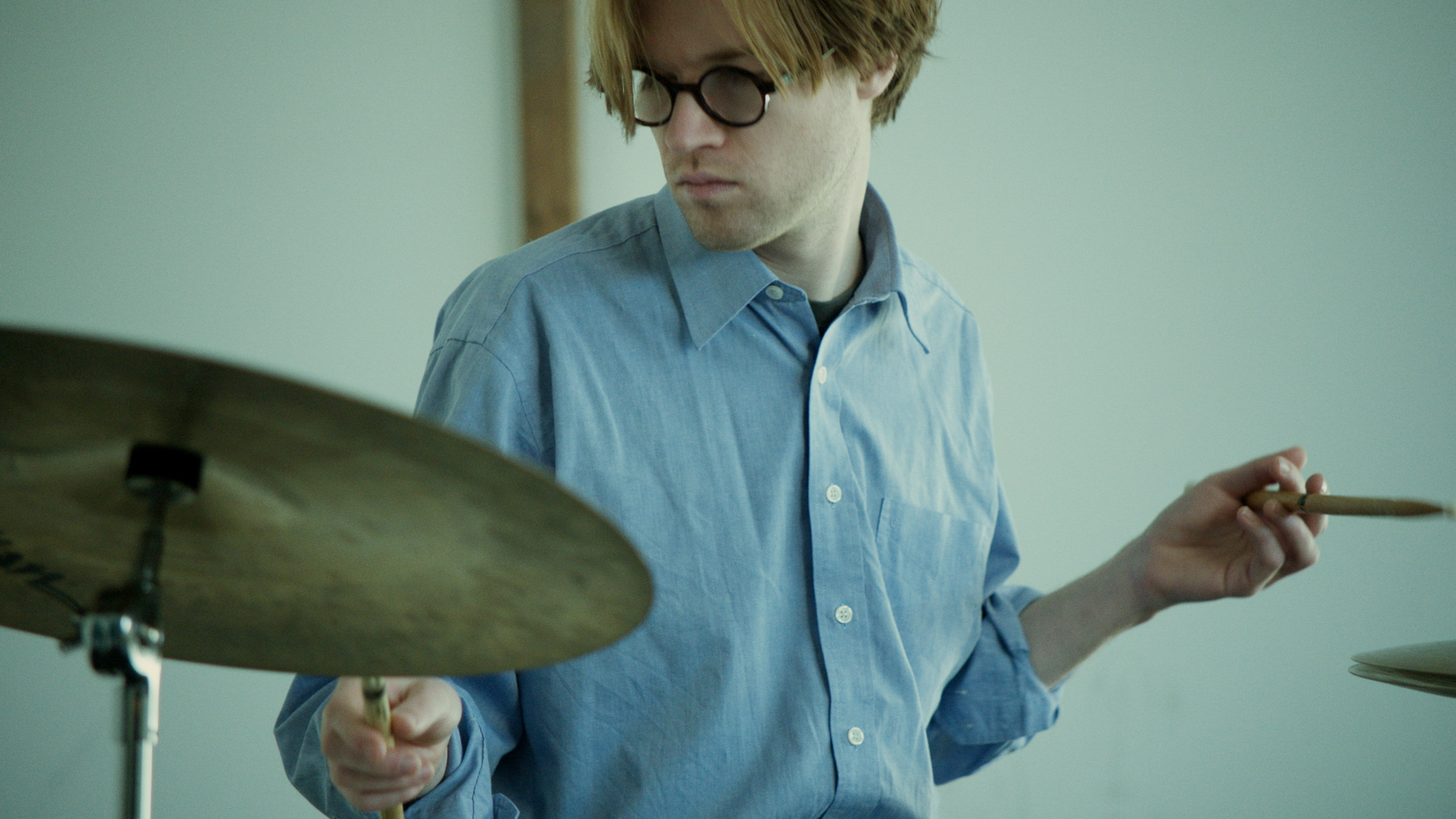 Mann mit Brille spielt Schlagzeug, hält einen Drumstick in der Hand.
