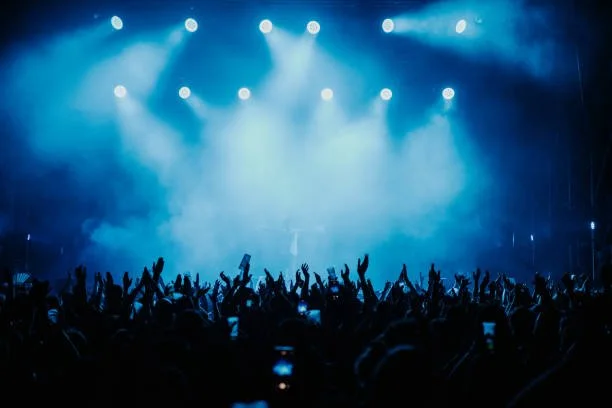 Crowd at a concert with raised hands under blue stage lights and fog.
