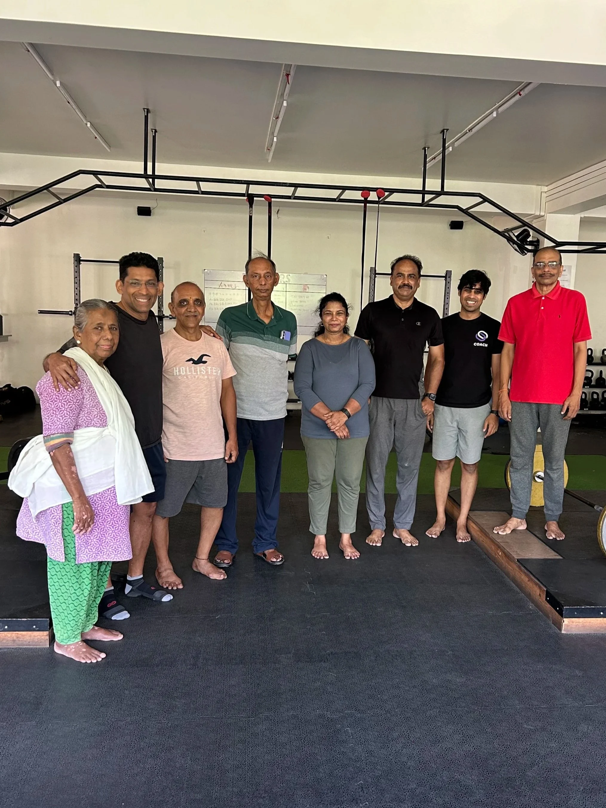 Chirag Chordia posing with a smiling group of senior fitness clients during a group training session inside a gym.