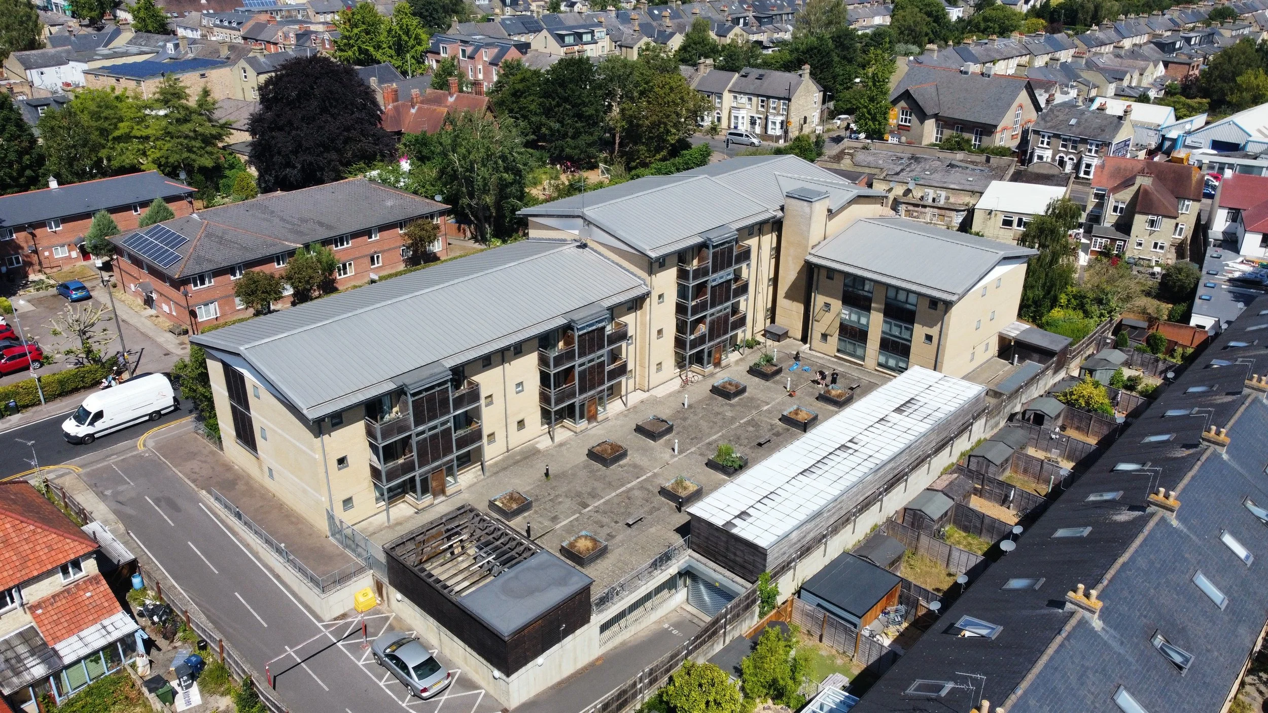 Aerial view of a modern residential building with a flat rooftop garden, surrounded by other homes and greenery in a suburban neighborhood.