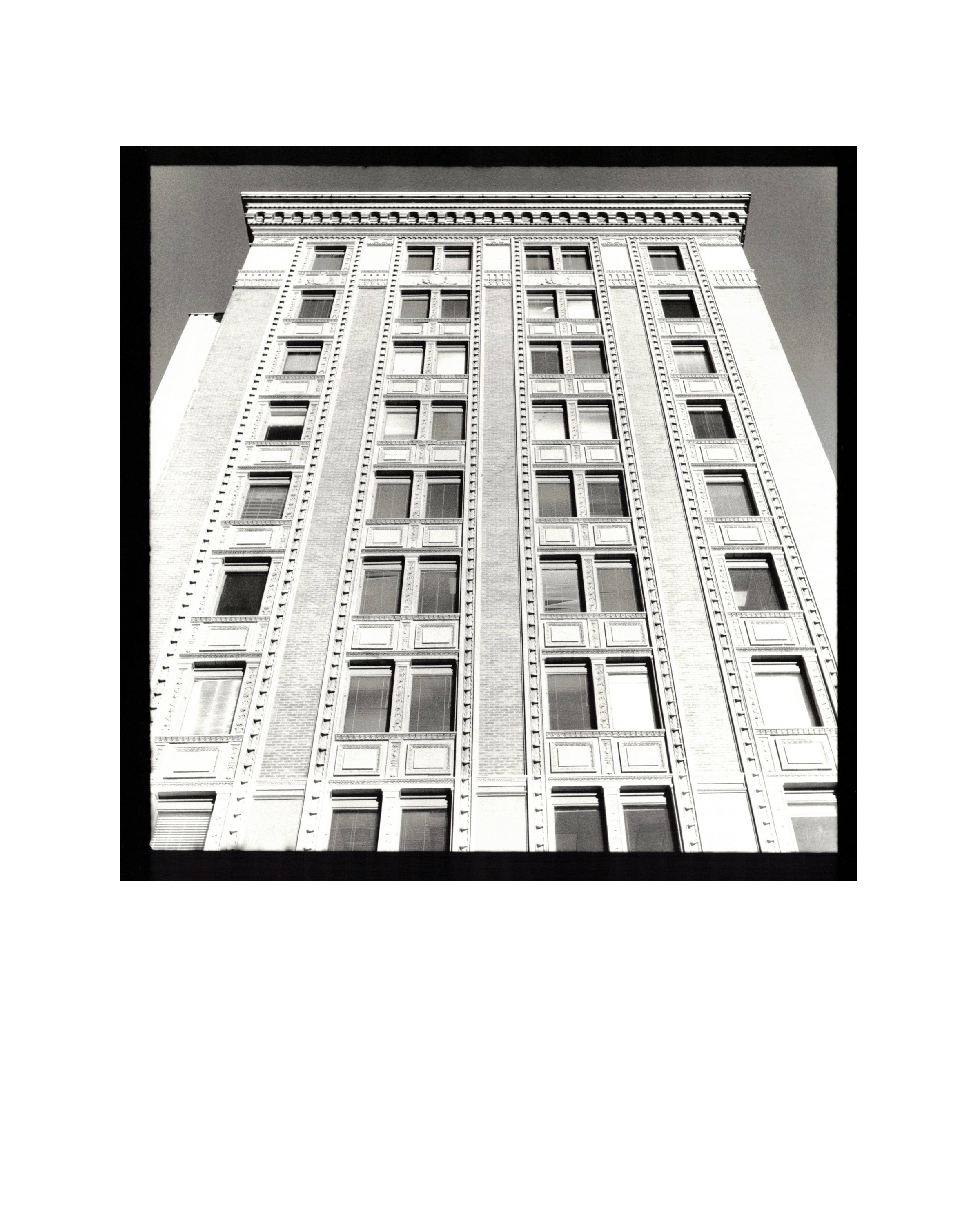 Black and white photo of a tall, ornate building with multiple windows, viewed from the ground up.