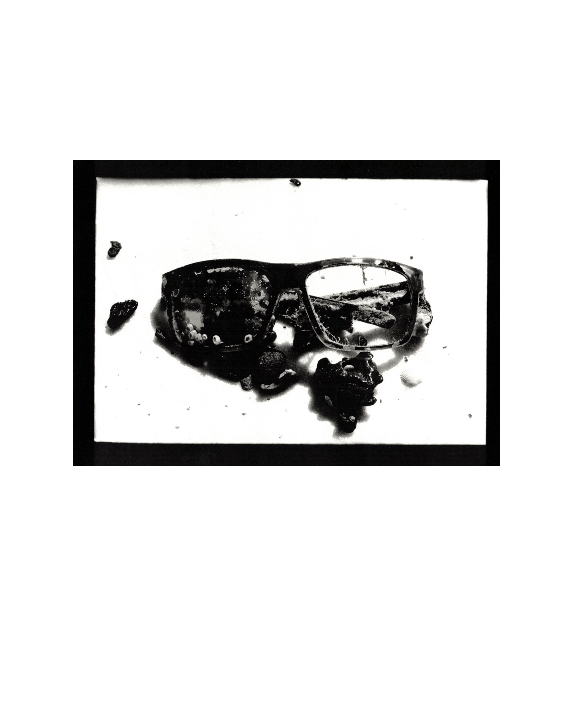 Black and white photo of a pair of sunglasses with some debris around them.