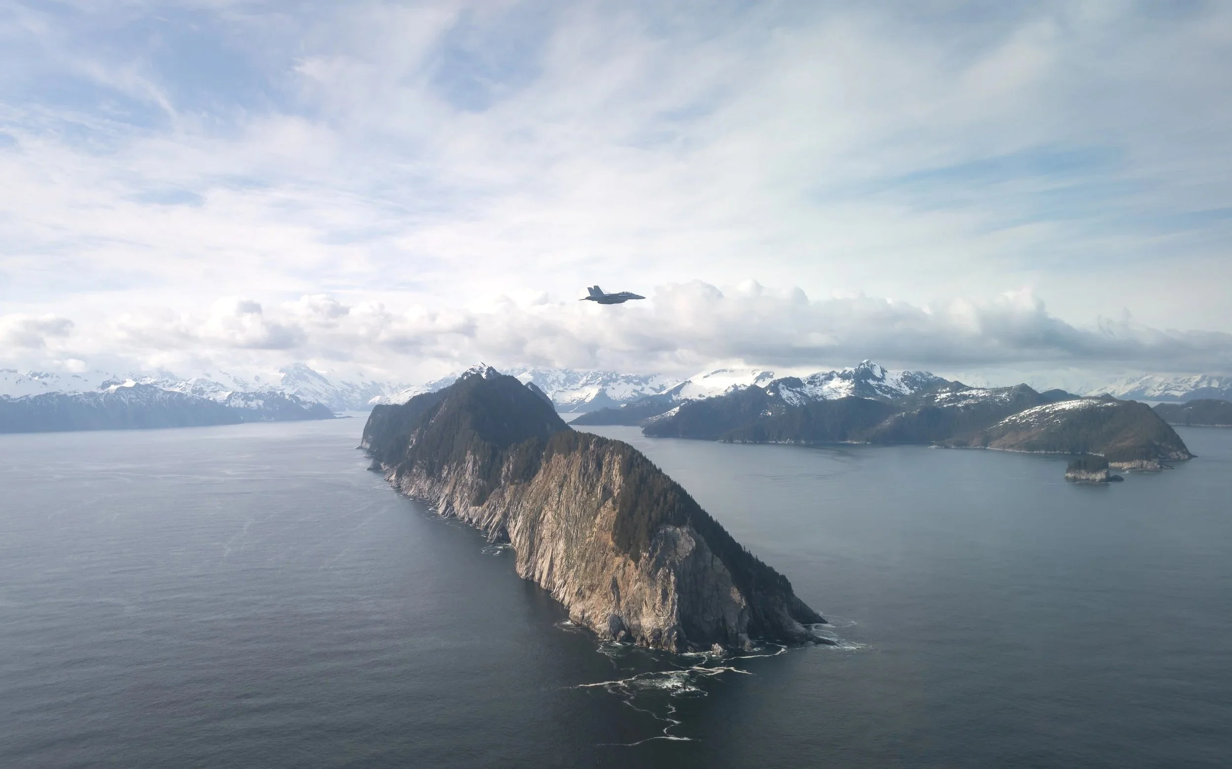 Photograph of jet flying over the water and mountains