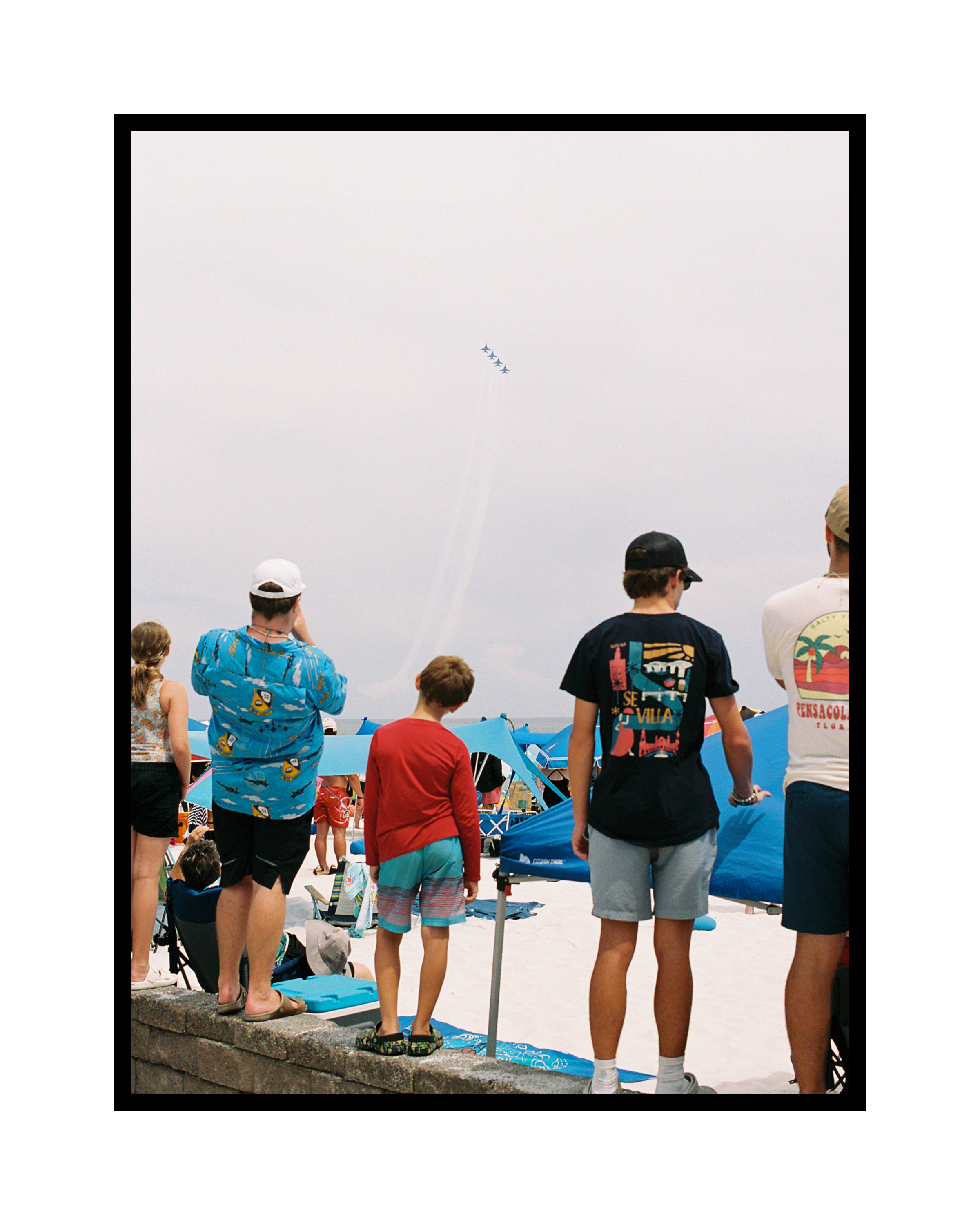 People at the beach watching an air show with the Blue Angel jets flying overhead in formation.