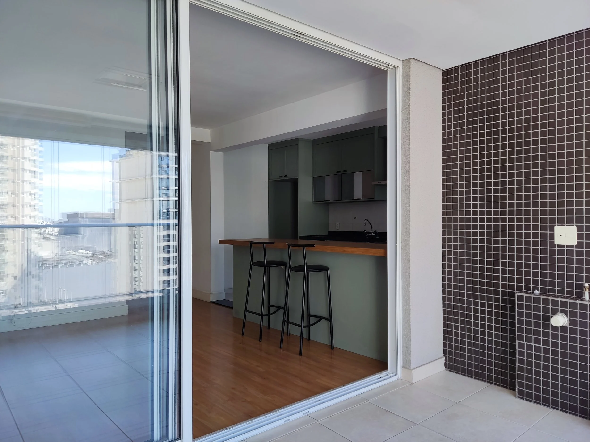 varanda com parede de azulejos escuros, espaço de lavar roupas com torneira e cuba