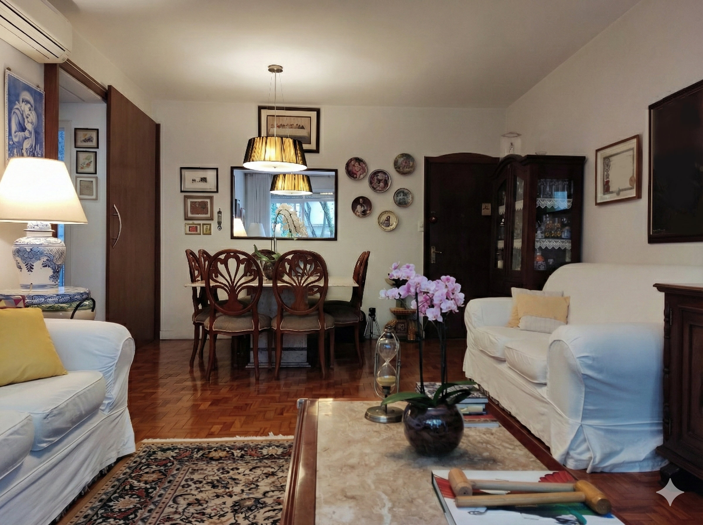 Sala de estar com sofá branco, mesa de centro de mármore, poltrona, plantas, iluminação de teto e várias obras de arte na parede.