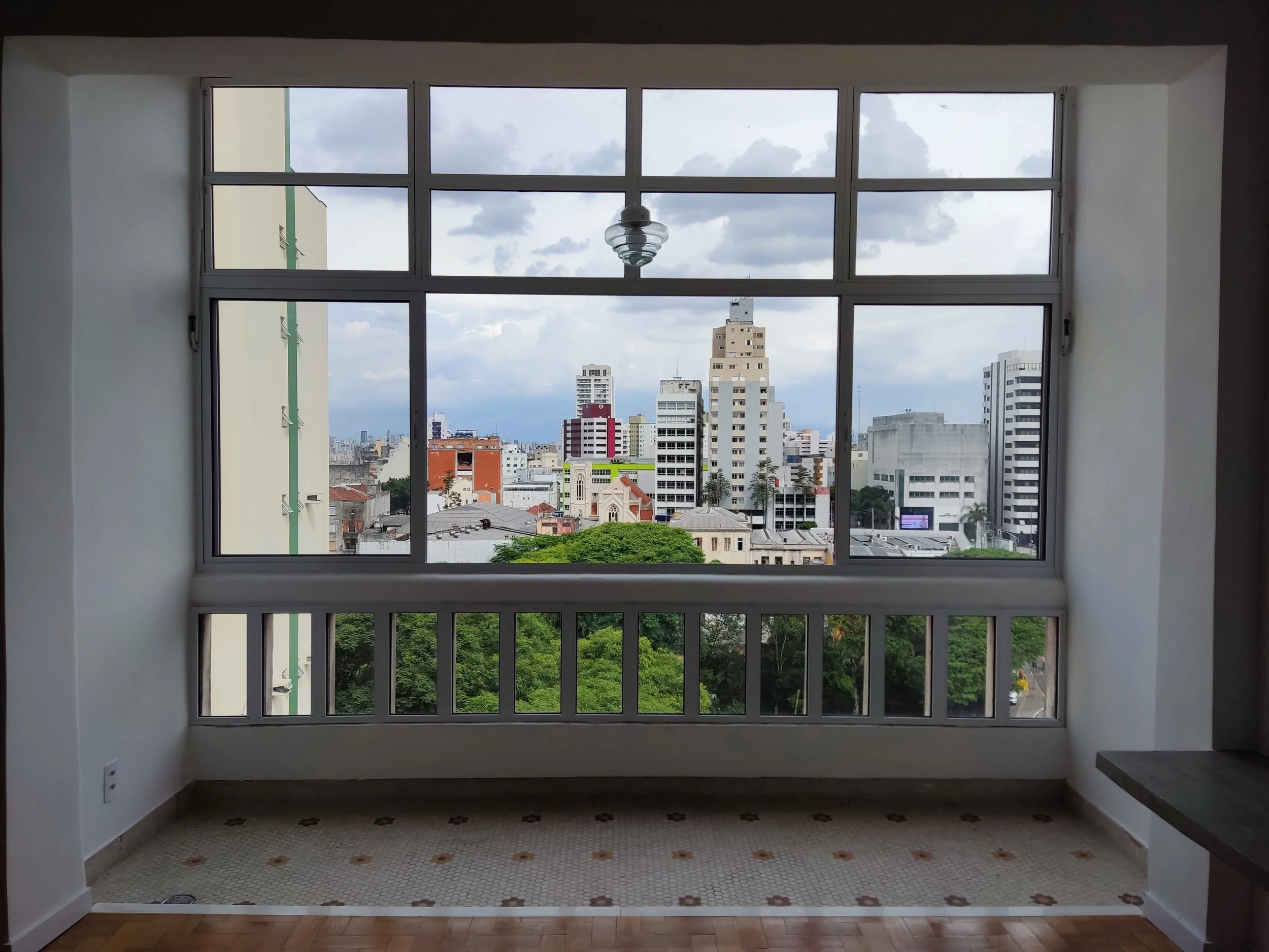 Vista de uma cidade a partir de uma janela grande, com prédios altos e céu parcialmente nublado.