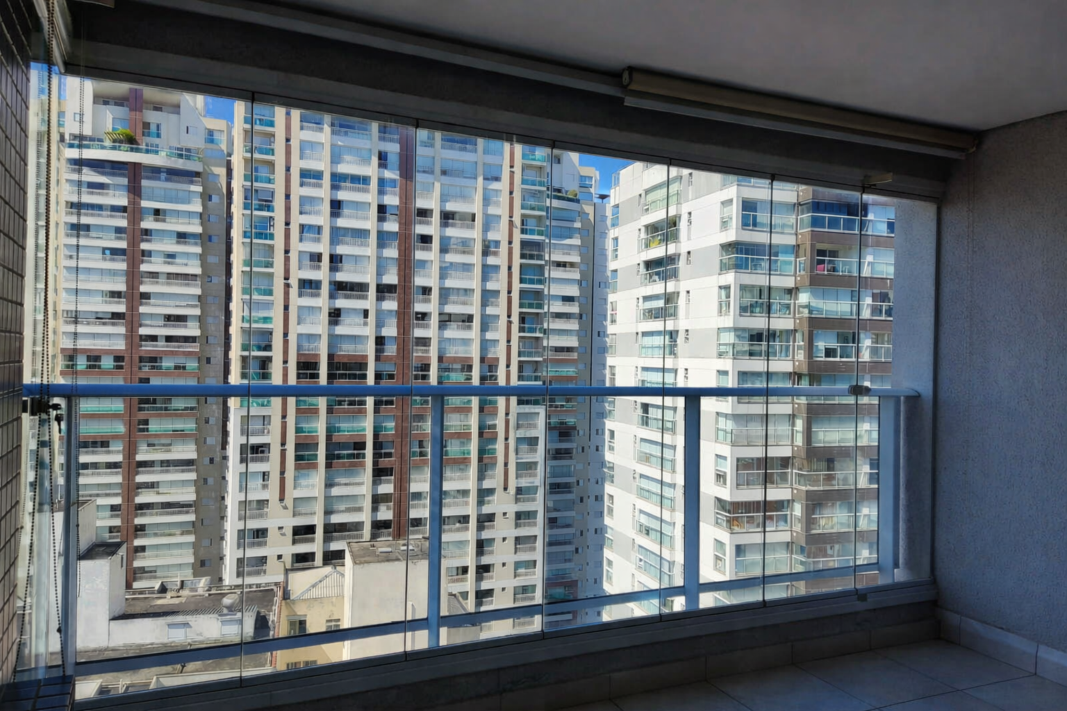 Vista de prédios altos de um apartamento com varanda de vidro.
