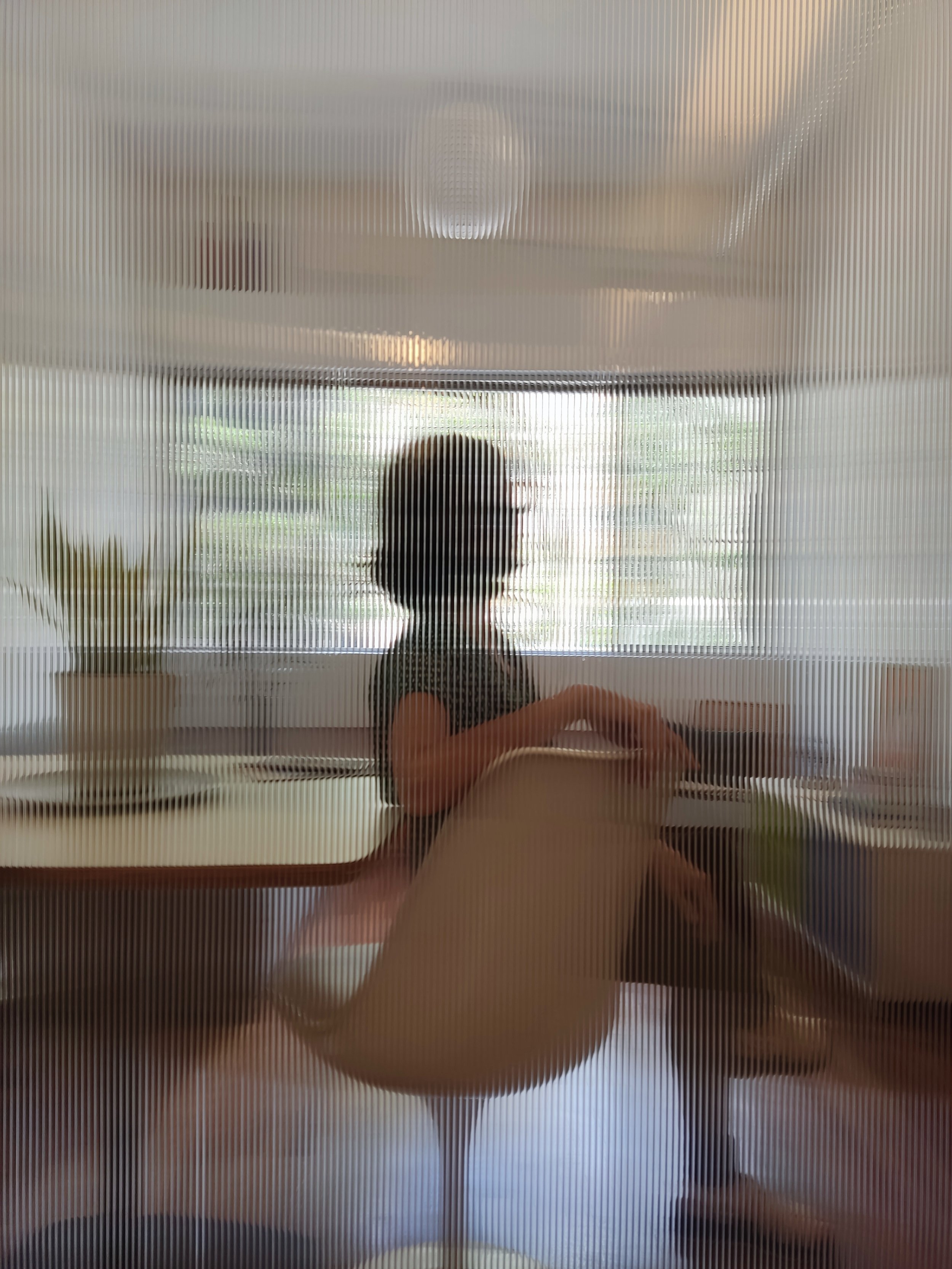 Silhueta de uma mulher de cabelos curtos sentada em uma cadeira no escritório, vista através de uma divisória de vidro fosco.