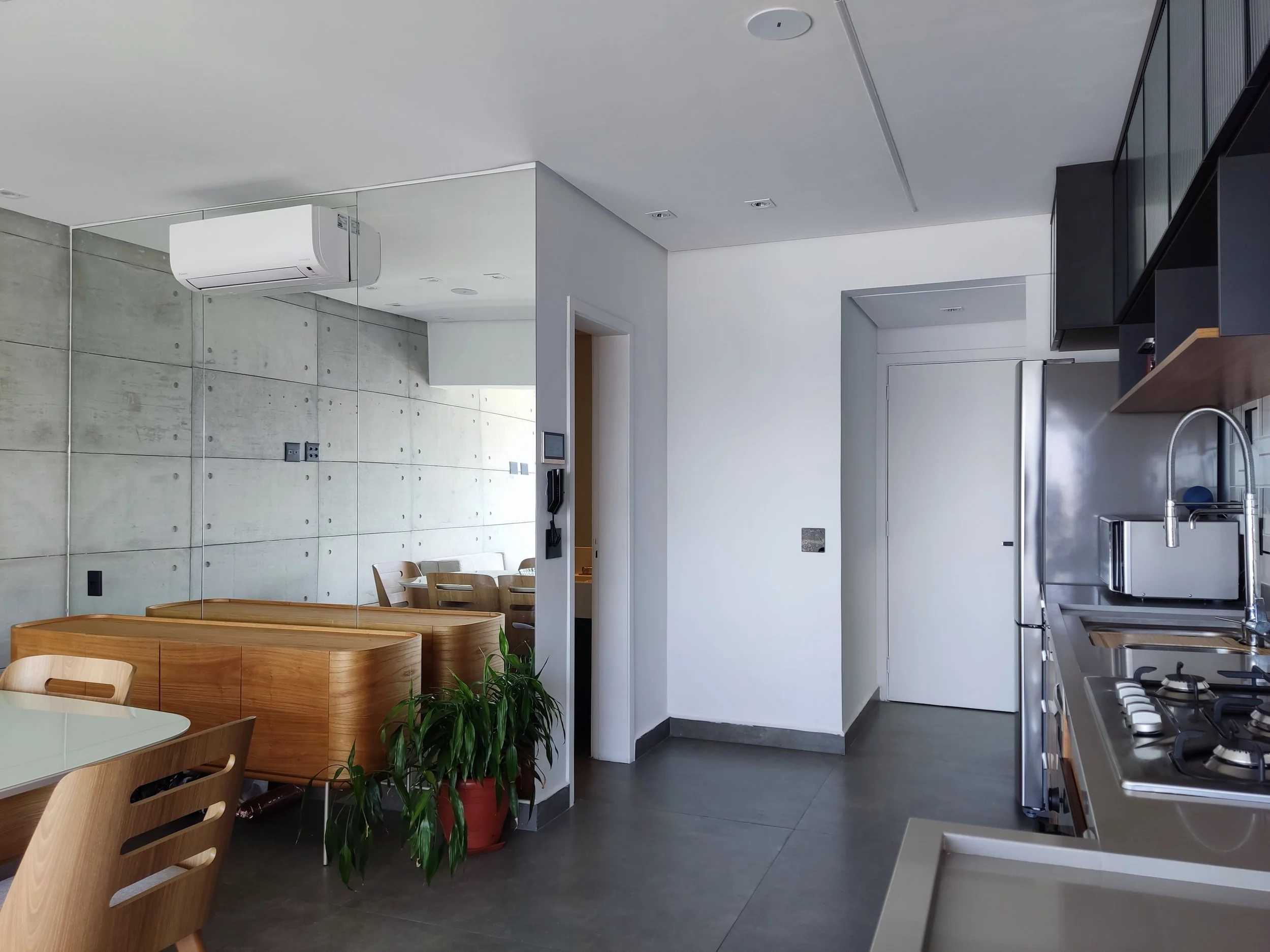 Cozinha moderna com paredes de cimento, eletrodomésticos de metal, mesa de jantar com cadeiras de madeira e uma plantação em vaso