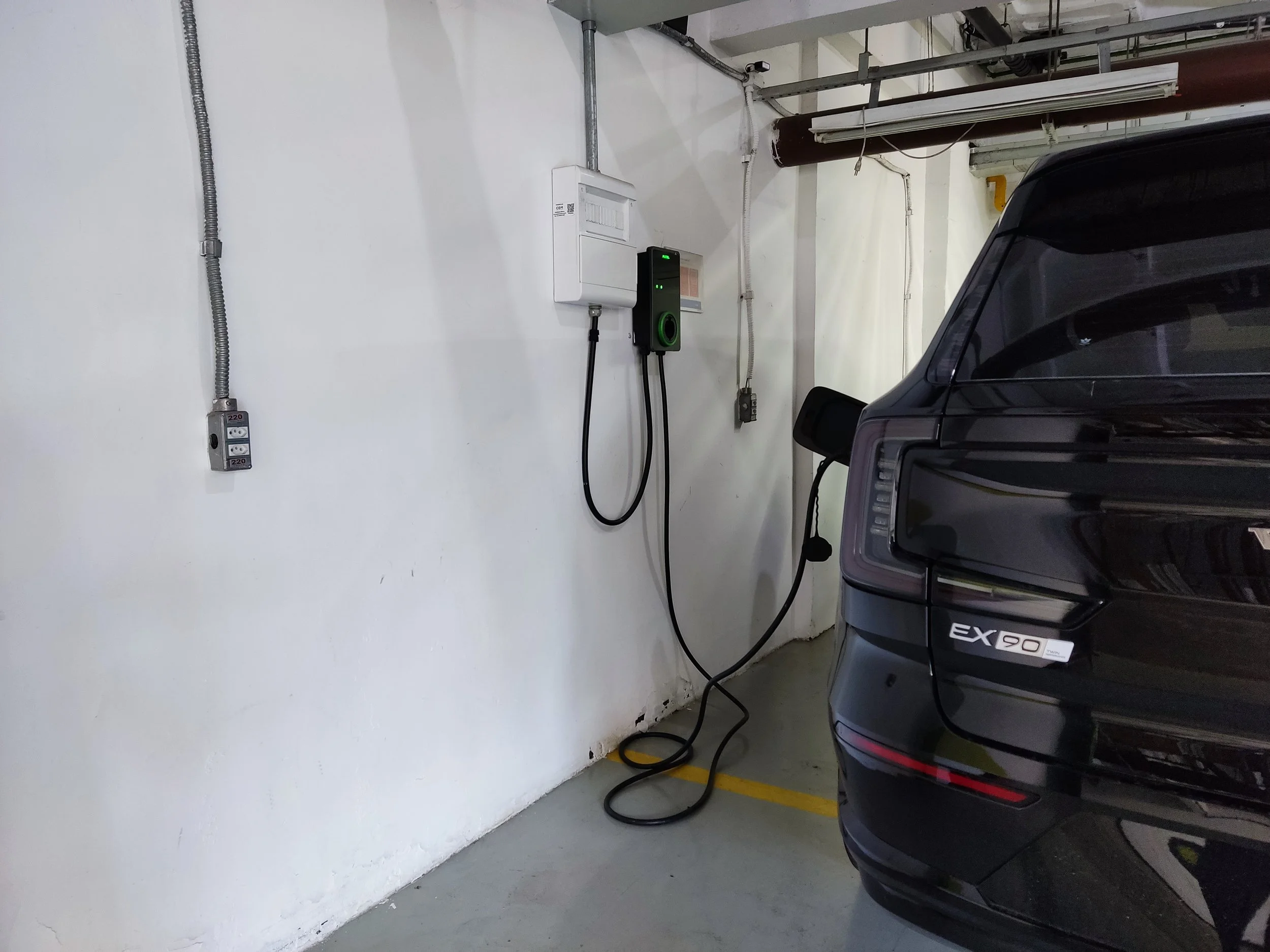 Estacionamento com carro preto e ponto de carregamento de veículo elétrico na parede.