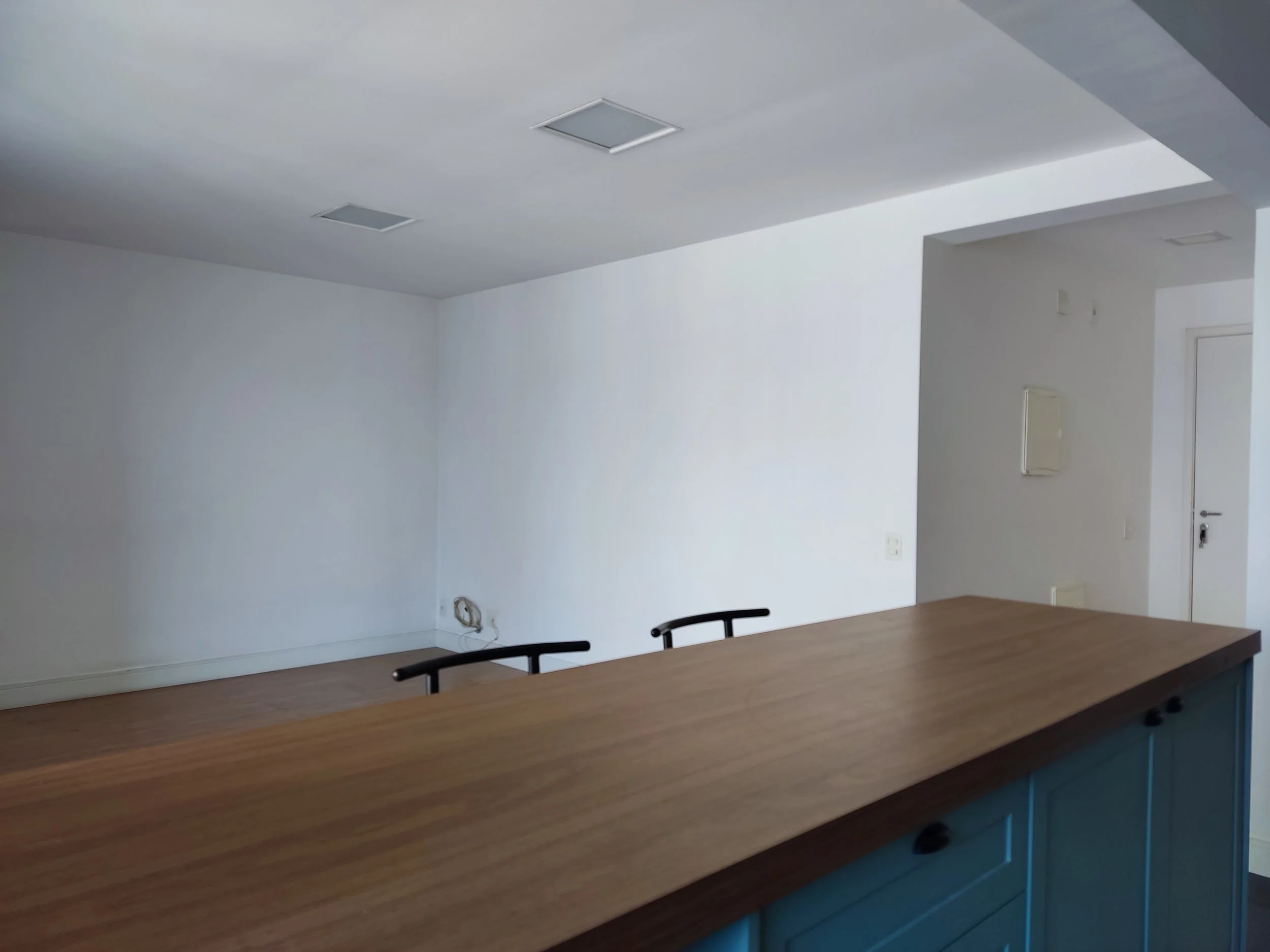 Sala vazia com piso de madeira, paredes brancas e uma bancada de madeira na frente