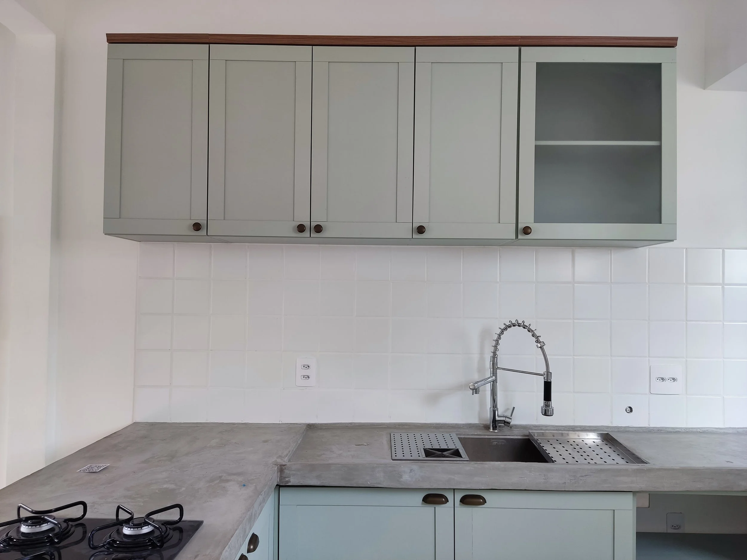 Cozinha com armários verdes, pia de aço inox, bancada de cimento e fogão com duas bocas.