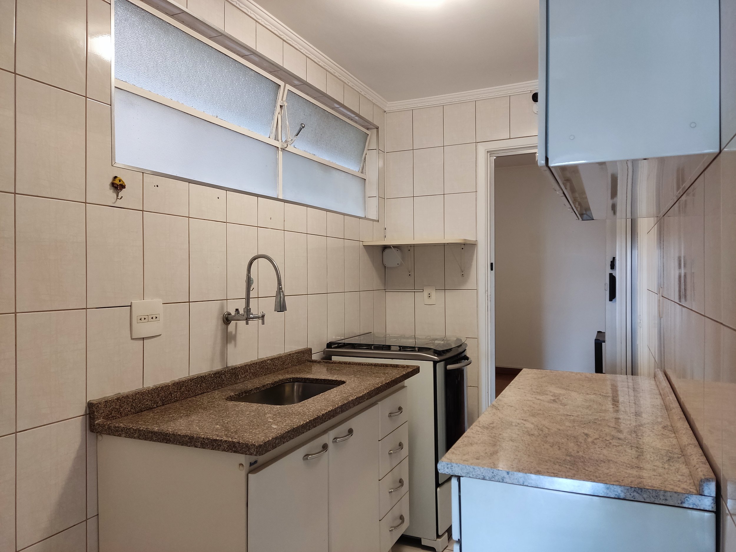 Cozinha com pia, fogão e armários, parede com revestimento de azulejos e janela de vidro fosco.