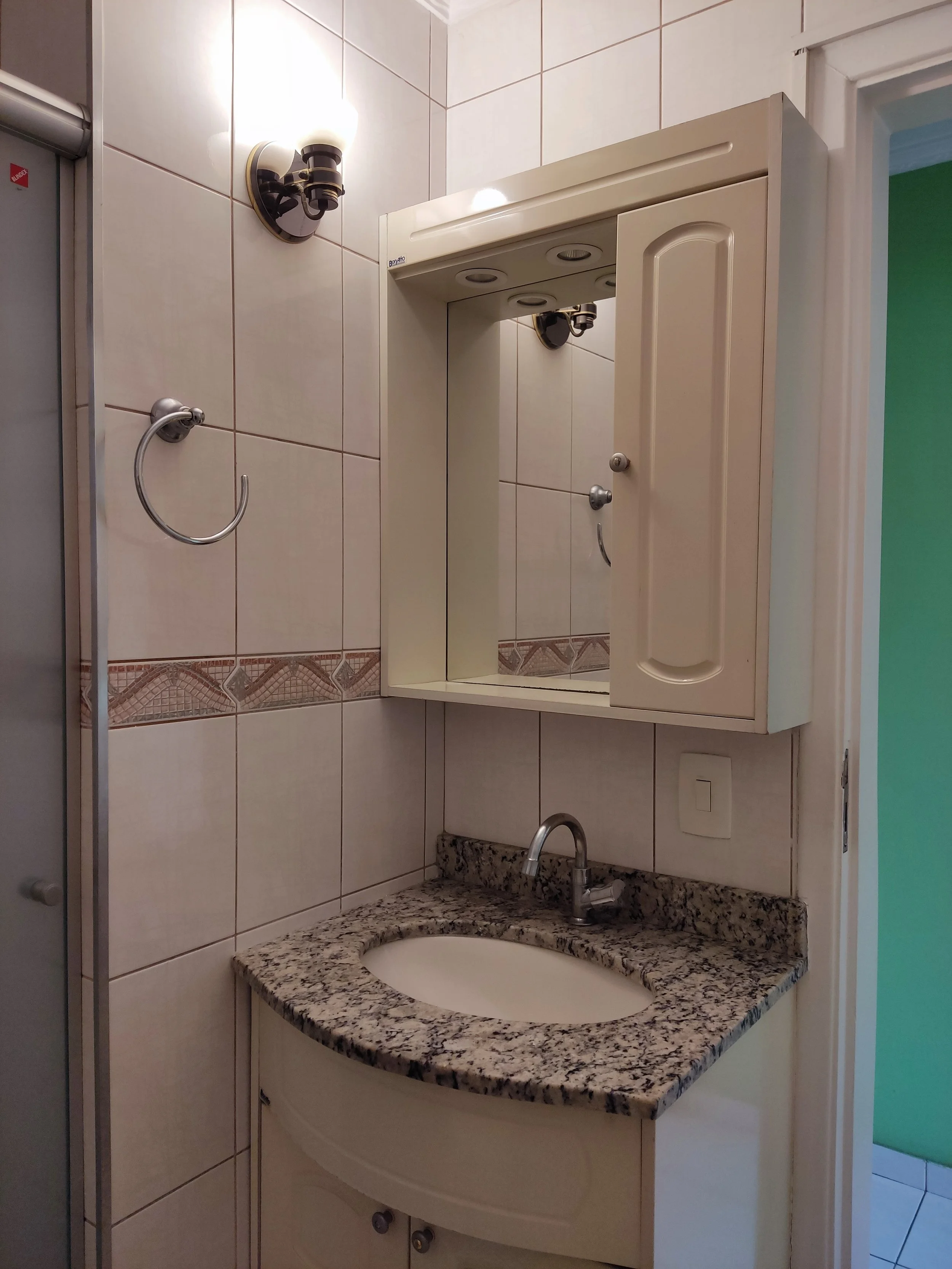 Espelho com gabinete de pia de granito em banheiro com paredes de azulejos brancos e luzes acima do espelho.