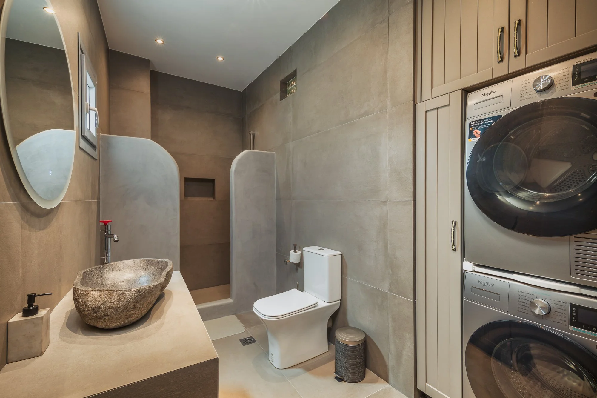 Modern bathroom with a stone sink, a toilet, a shower area with privacy divider, washing machine, and dryer stacked, and a mirror on the wall.