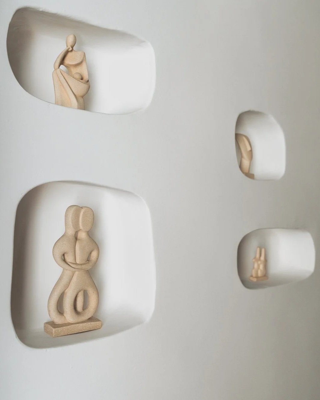 Wooden abstract sculptures displayed in wall cutouts, representing human and animal figures.