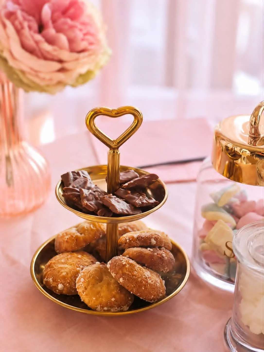 Plate à deux étages avec biscuits et chocolat, décoration de fête rose et dorée.