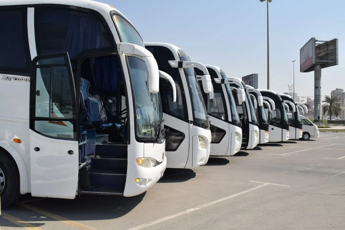 Multiple white tour buses parked in a lot under a clear sky.