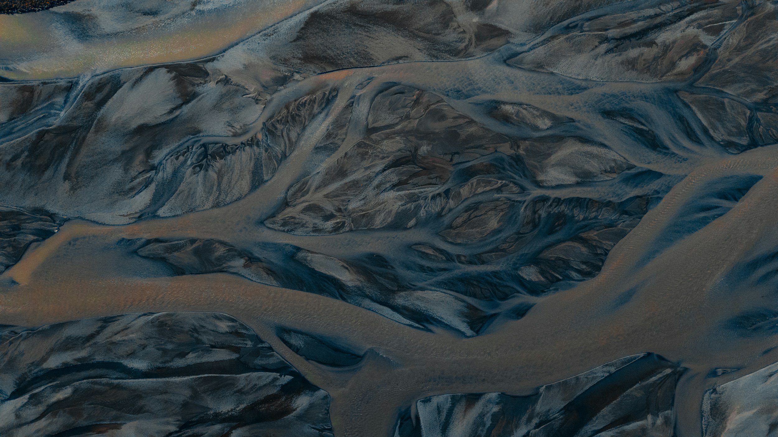 Aerial view of a mountainous landscape with winding rivers and dark, rugged terrain.