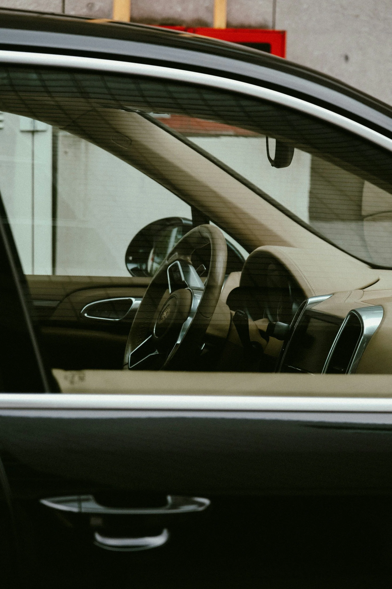 Close-up of the interior of a luxury car, showing the steering wheel, dashboard, and front seat, viewed through the passenger side window.
