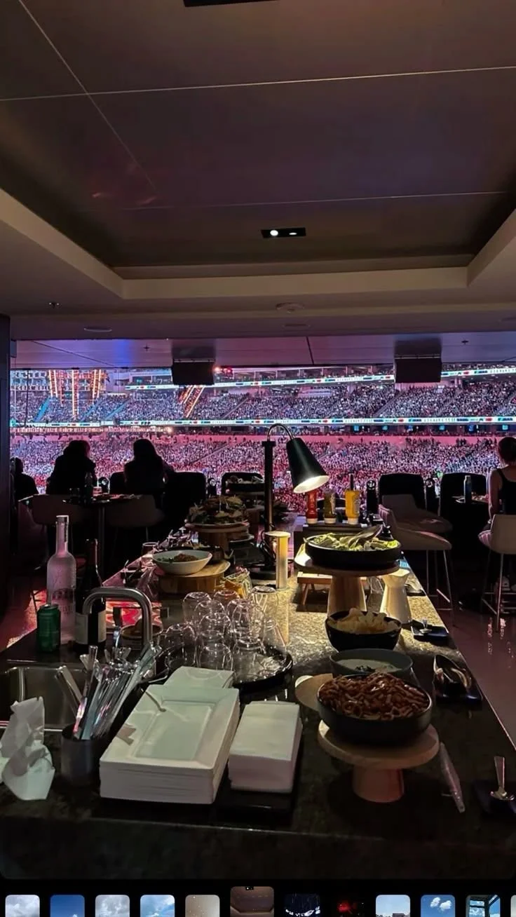 View of a crowded stadium from inside a restaurant with food and drinks on the table in the foreground.