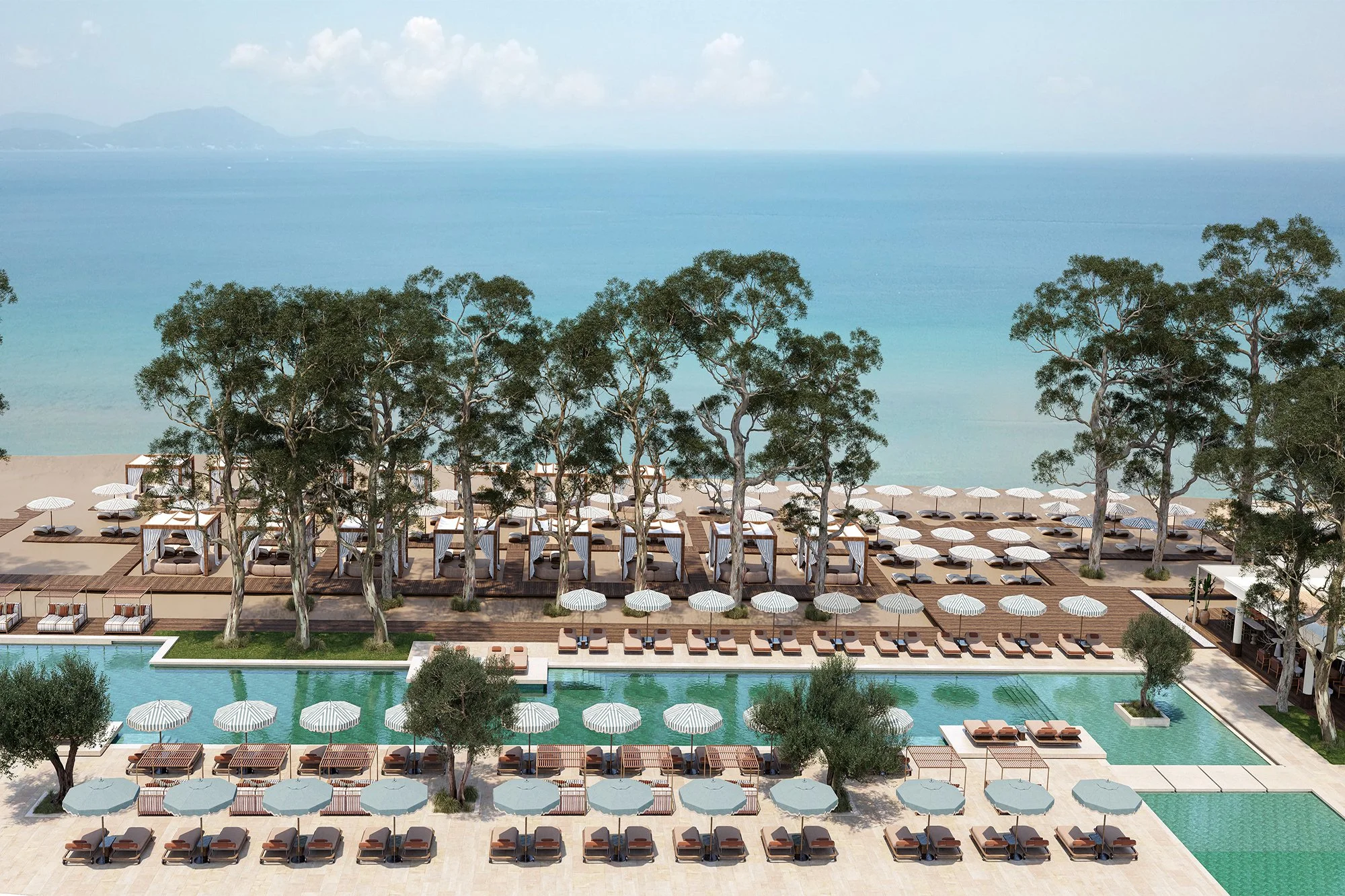 Aerial view of a luxurious outdoor pool area with lounge chairs and umbrellas, surrounded by trees with an ocean view in the background.