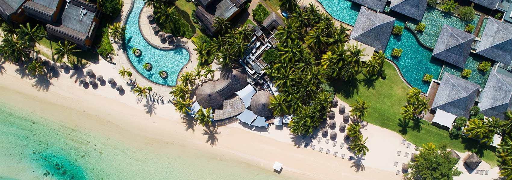 Aerial view of a tropical resort with a beach, swimming pools, palm trees, and resort buildings.