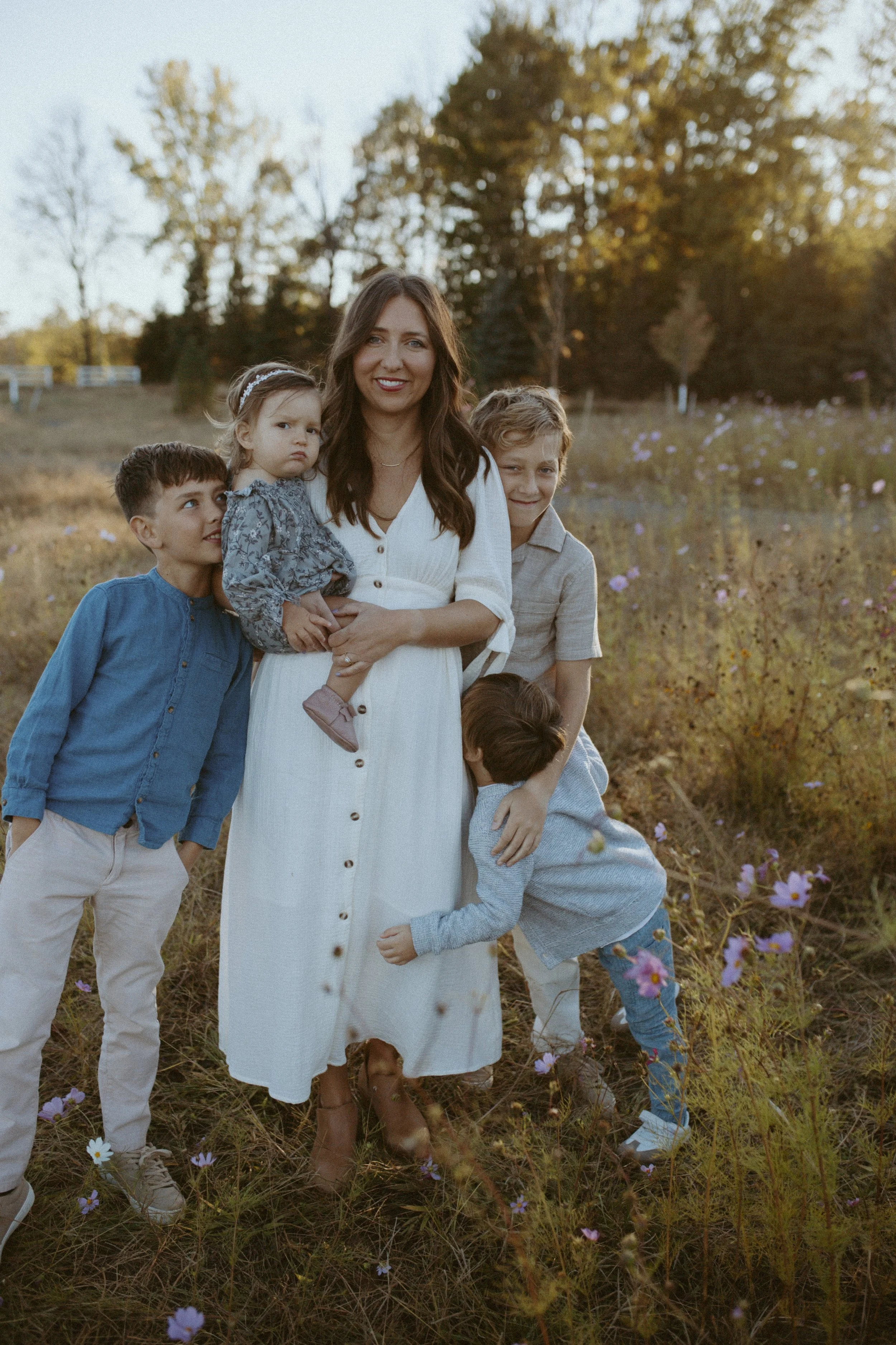 A woman with four children standing in a field of pink and purple flowers during sunset, with trees in the background.