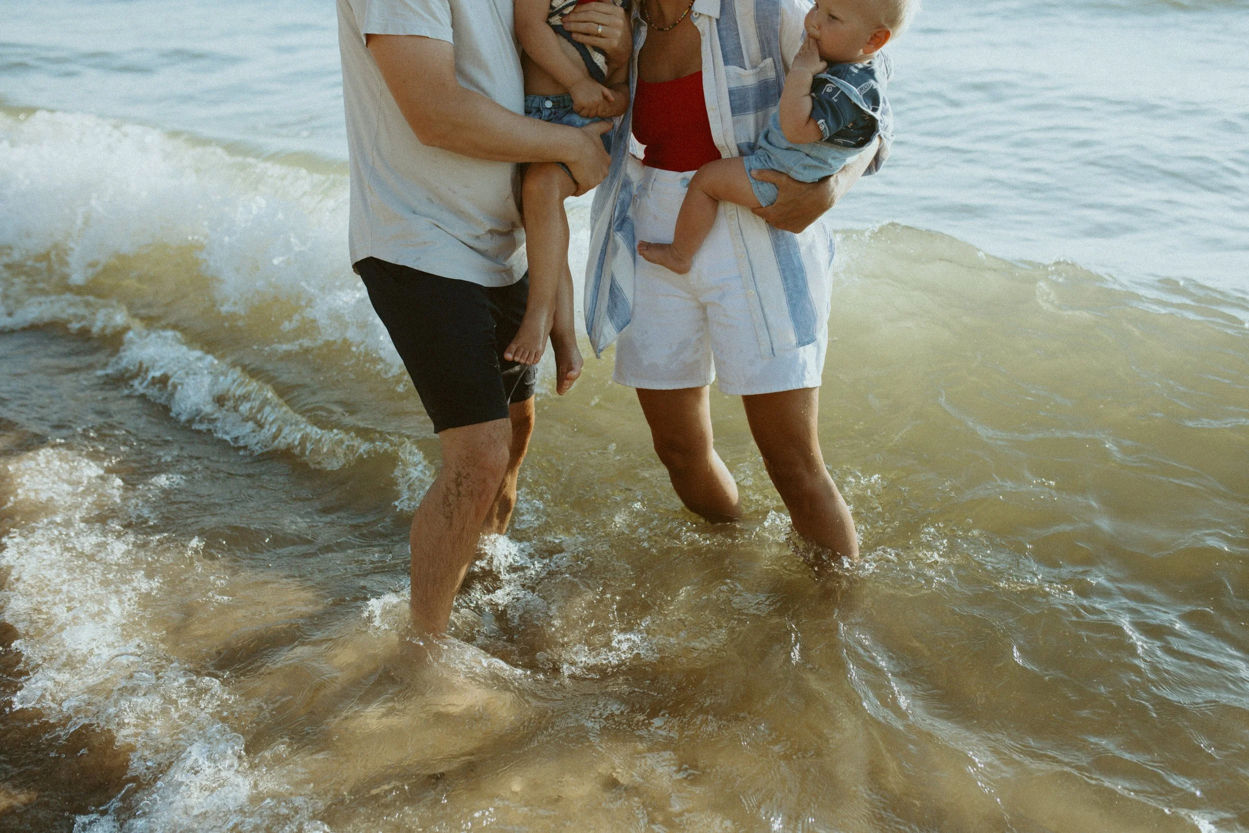 A family standing in lake Michigan, with two children and adults holding hands and feet as they enjoy the water.