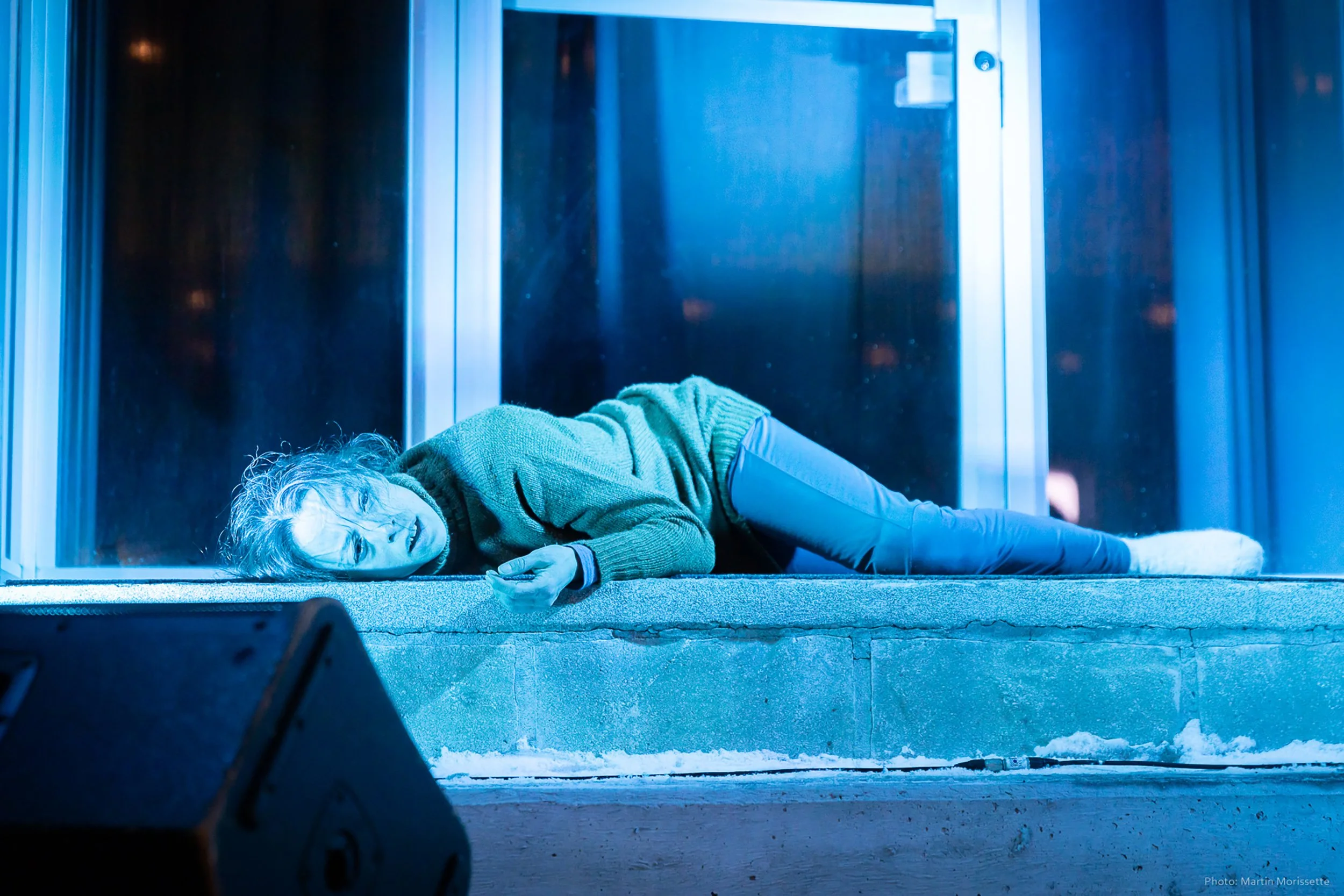 A person lying on the ground, appearing distressed or unconscious, on a small porch with a speaker in the foreground.