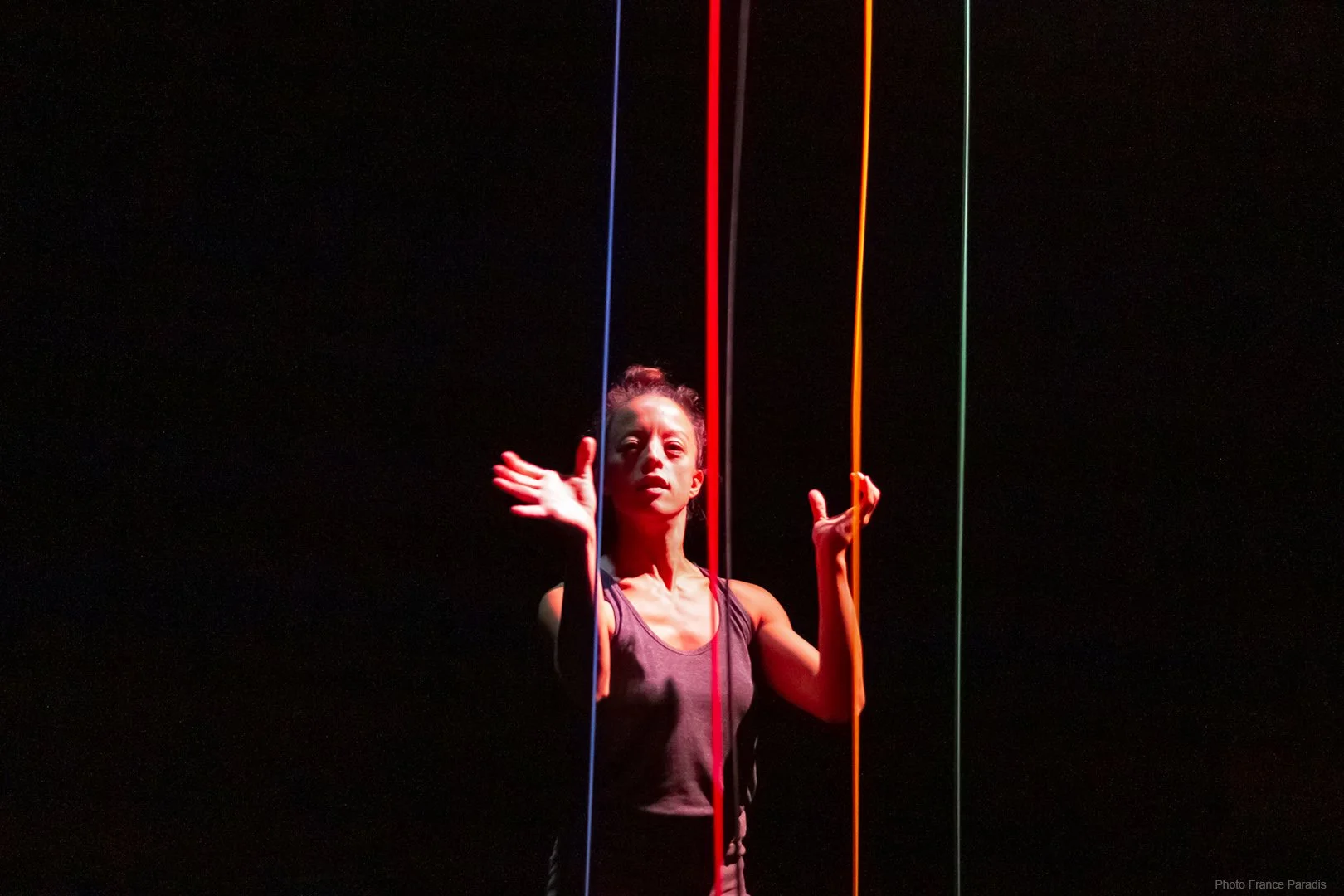 A woman performing on stage with dark background, illuminated by colorful vertical light rods in red, blue, yellow, and green.