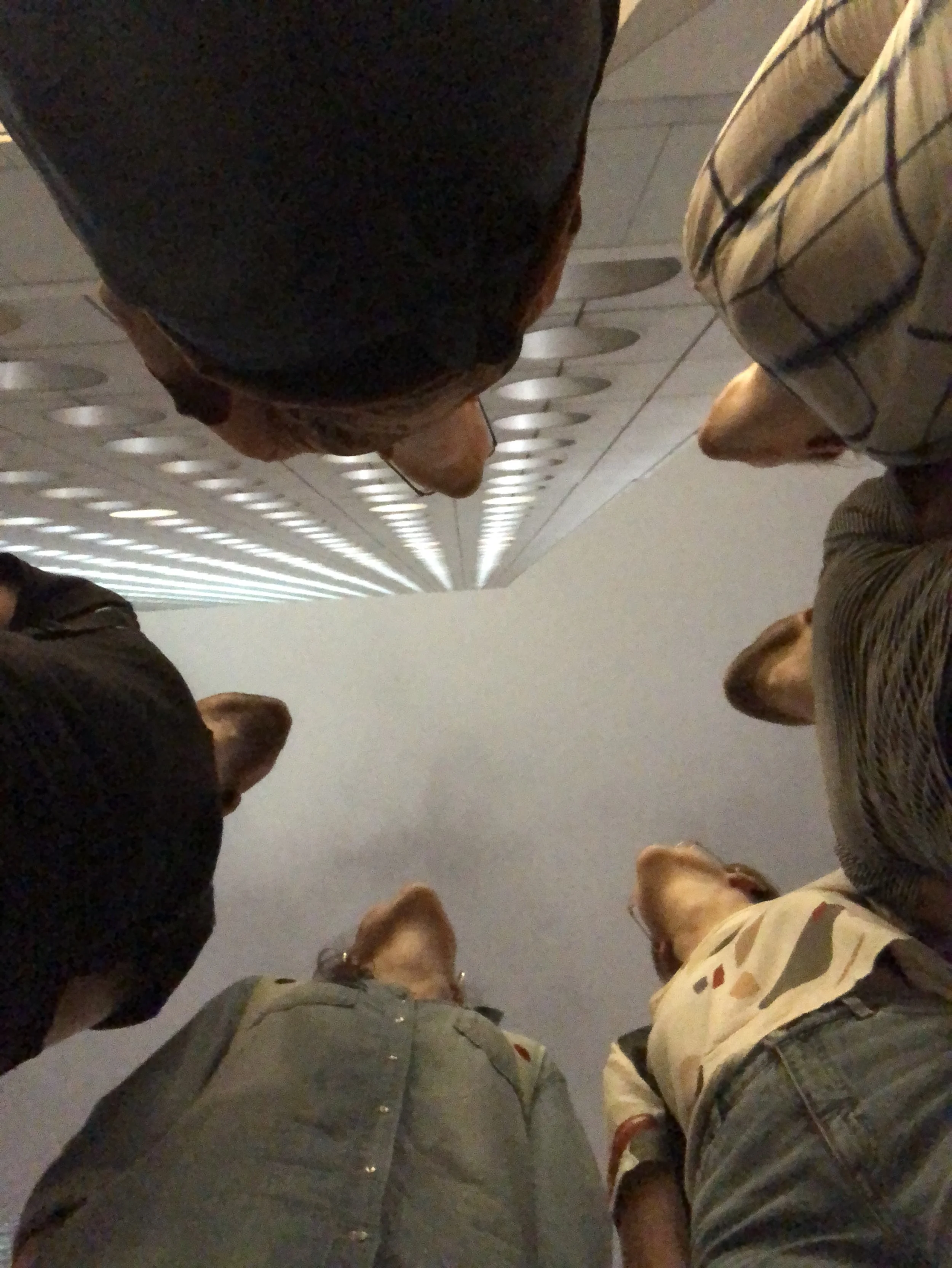 Een groep mensen zit op de grond en kijkt omhoog, de foto is genomen vanaf de grond gericht naar het plafond.