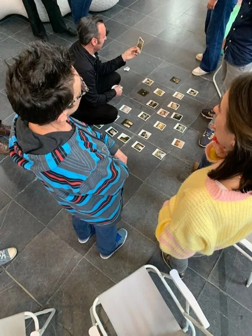 Mensen die een kaartenspel spelen op de vloer, met vier mensen die ernaar kijken en één persoon die een kaart vasthoudt.