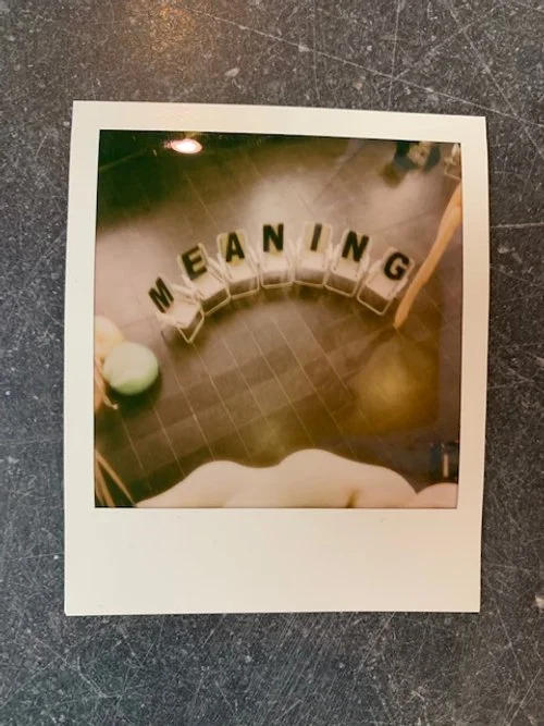 Fotografie van een bord met de woorden 'MEANING', dat is gemaakt met metalen letters op een vloer, met een stok en een groene bal ernaast.