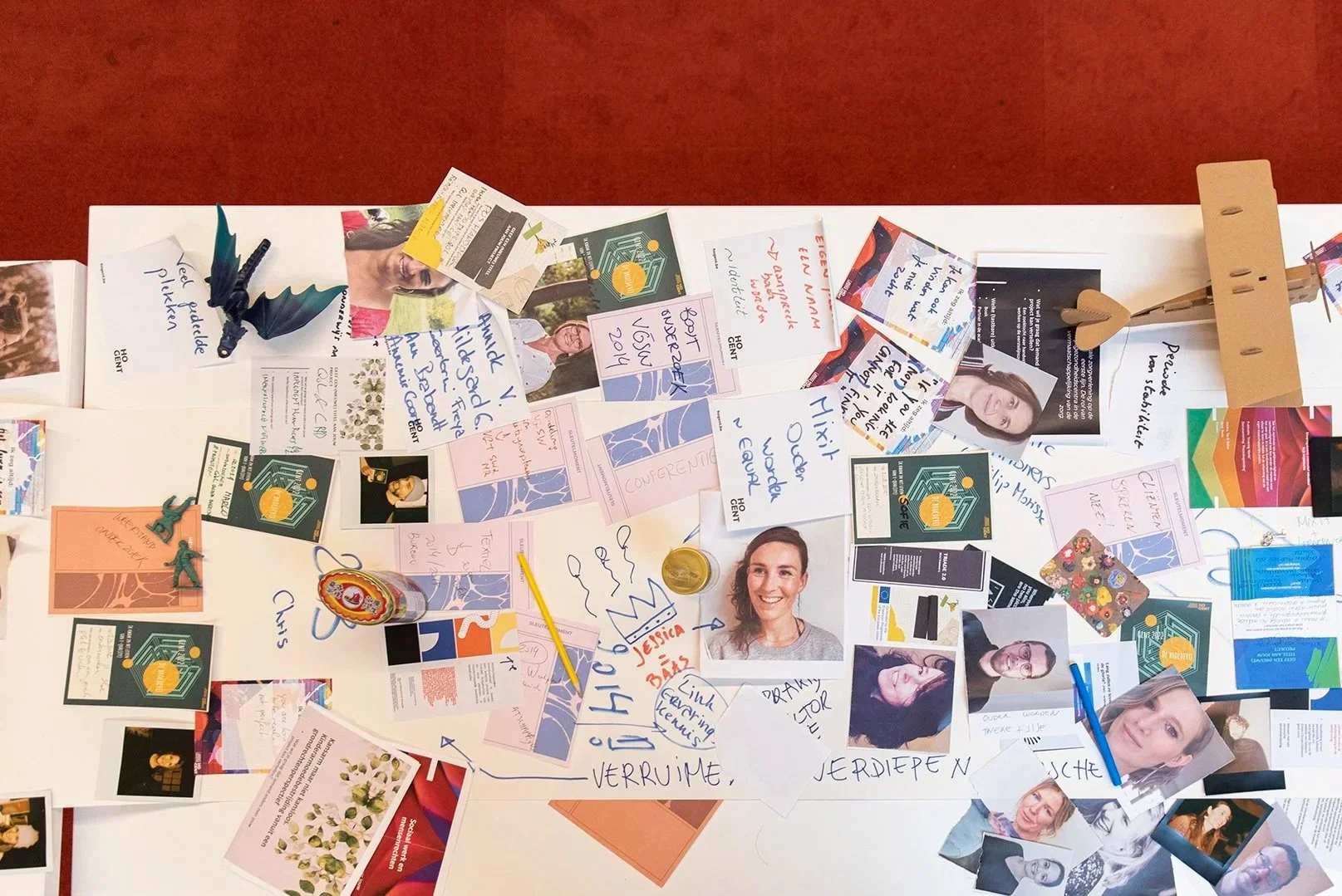 Een collage van foto's, notities, kaartjes en kleine voorwerpen op een witte tafel, met foto's van mensen en diverse handgeschreven berichten.