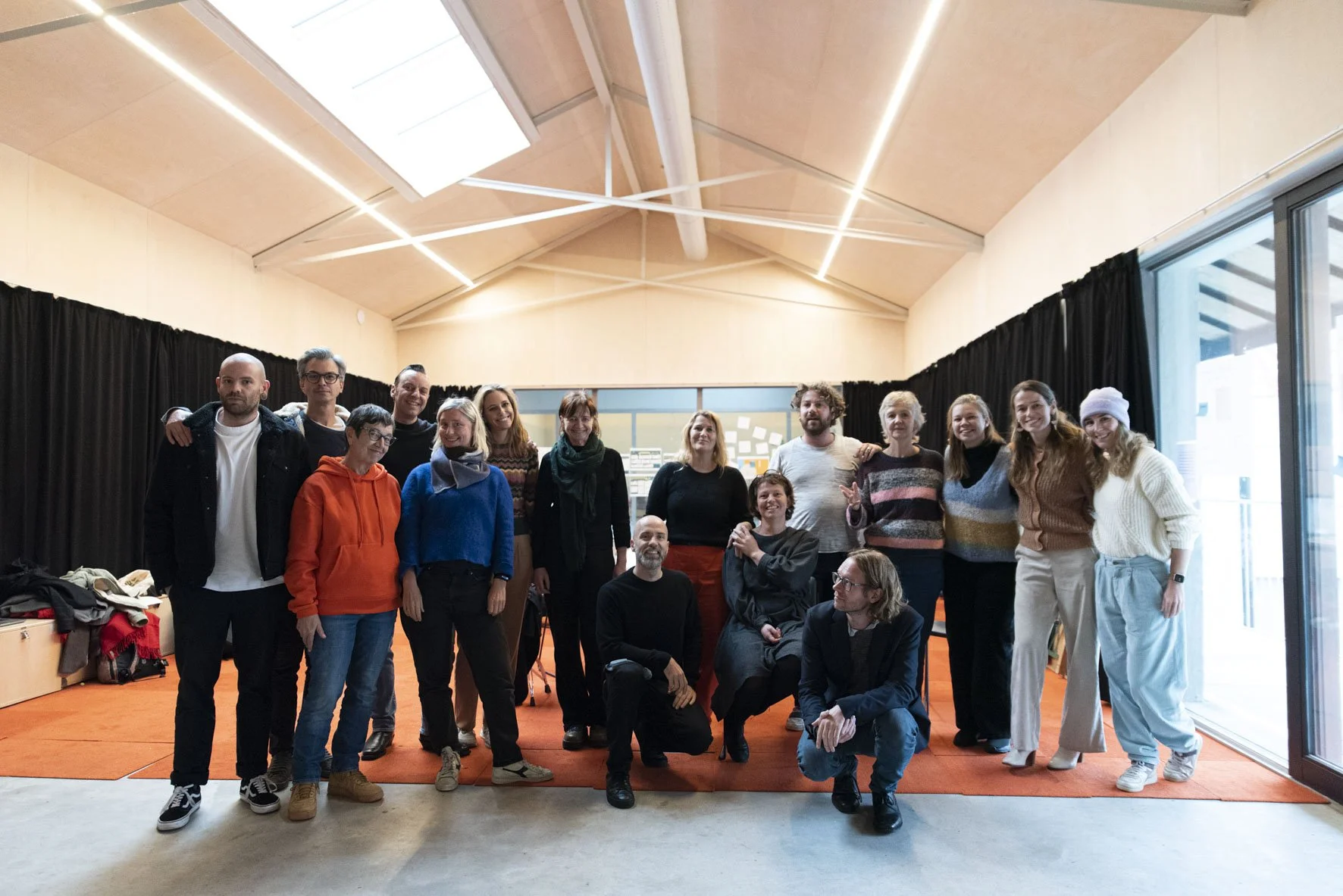 Vereenvoudigde foto van een groep mensen die samen in een kamer staan, achter hen zwarte gordijnen en een muur met post-its.