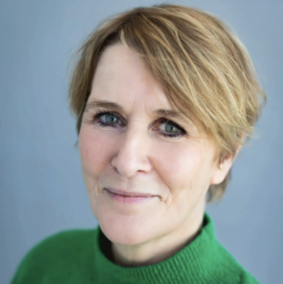 Portret van een vrouw met korte, lichtbruine haar in een groene trui, lachend en kijkend naar de camera.