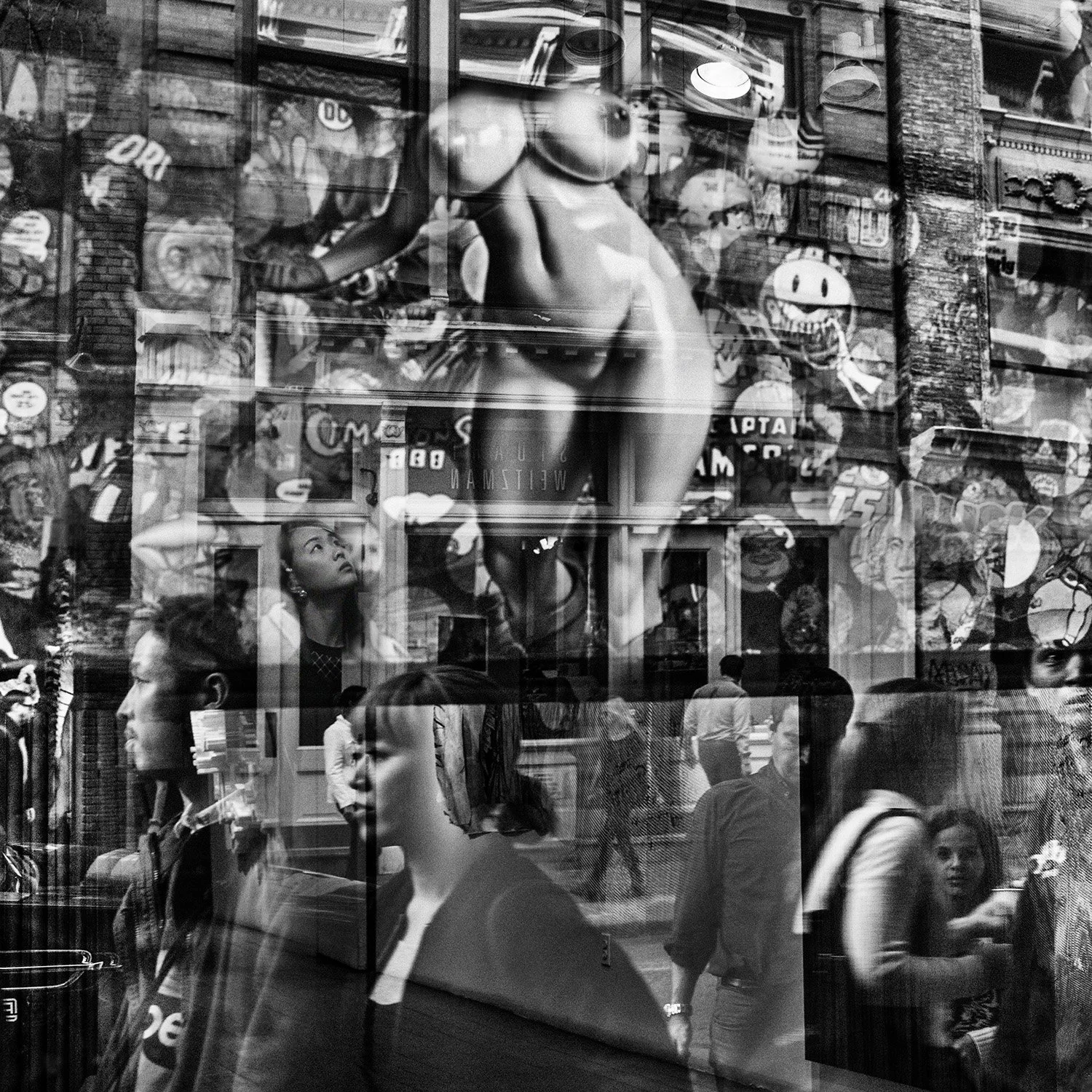Street scene with multiple pedestrians, reflection of storefront with cartoon artwork, including a large illustration of a woman and vintage advertisements in black and white.