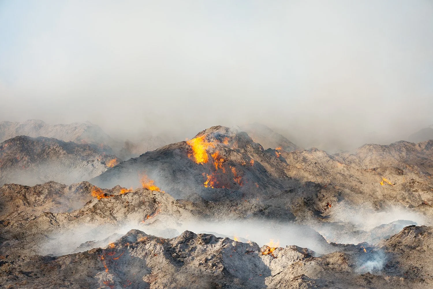 Volcanic eruption with lava flowing down rocky mountains, smoke and ash in the air.