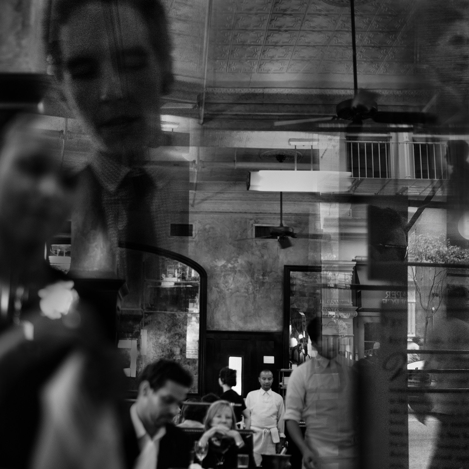Reflection of a woman taking a photo in a restaurant window with other people dining inside.
