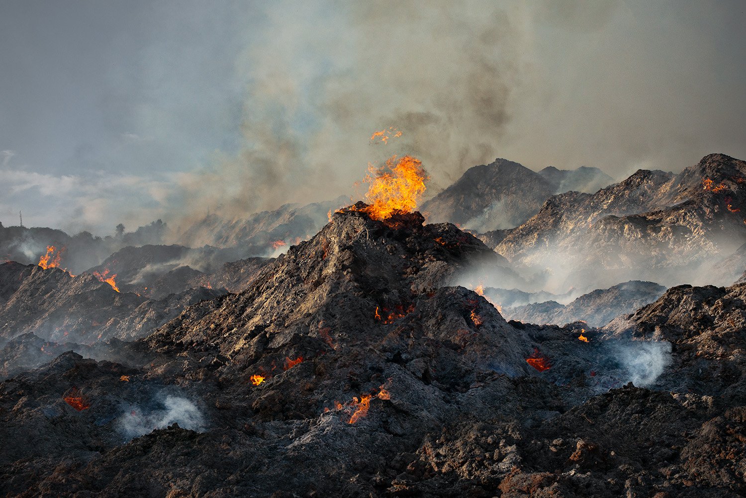 Volcano with flowing lava and smoke rising from the rugged, dark landscape.