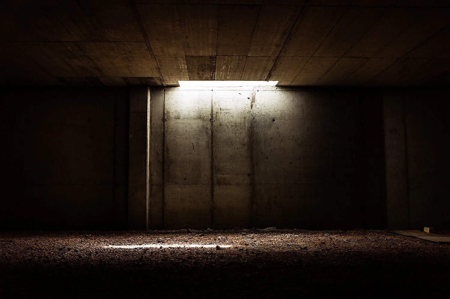 Underground parking garage with concrete walls and ceiling, illuminated by natural light from an opening at the top.