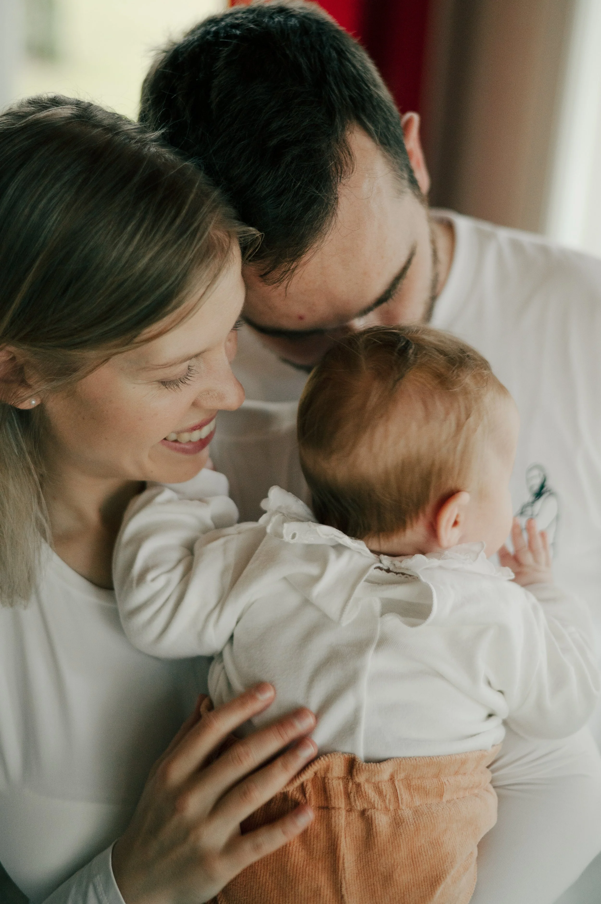 Perhe, jossa on kaksi aikuista ja lapsi, lähekkäin ja hymyilemässä.