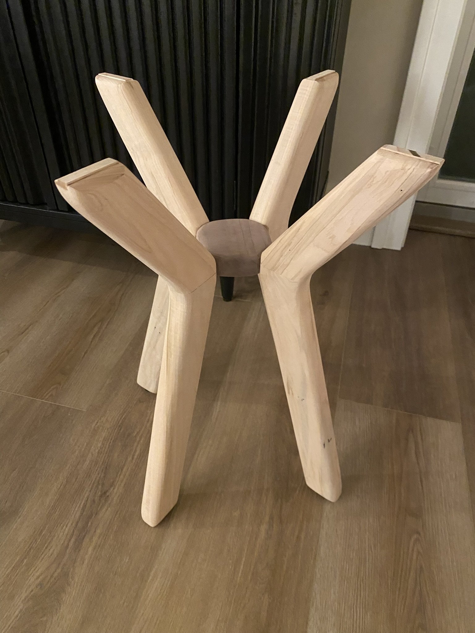 Unfinished wooden chair with four legs and a round seat, positioned upside down on a wooden floor.